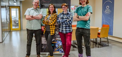 Figure 1: Four physicists pose in front of a HIP information banner, in the hallway of the Physicum building. They all have crossed arms and are laughing at the camera.